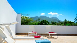 A rooftop terrace with white lounge chairs and red and blue towels, overlooking a mountainous landscape. - Rosil Place (Puerto Plata)