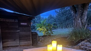 Un bar extérieur en bois, agrémenté de trois bougies allumées, de deux tabourets en bois et d’une base en briques.