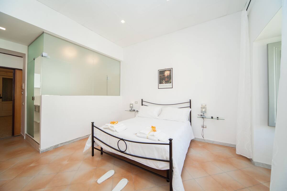 A neatly arranged bedroom with a bed, bedside lamps, and a mirror on the wall.