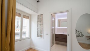A room with a wooden floor, a window with a view of a balcony, a door leading to a bathroom, and a mirror on the wall. - Eugenia e Donato (Naples)