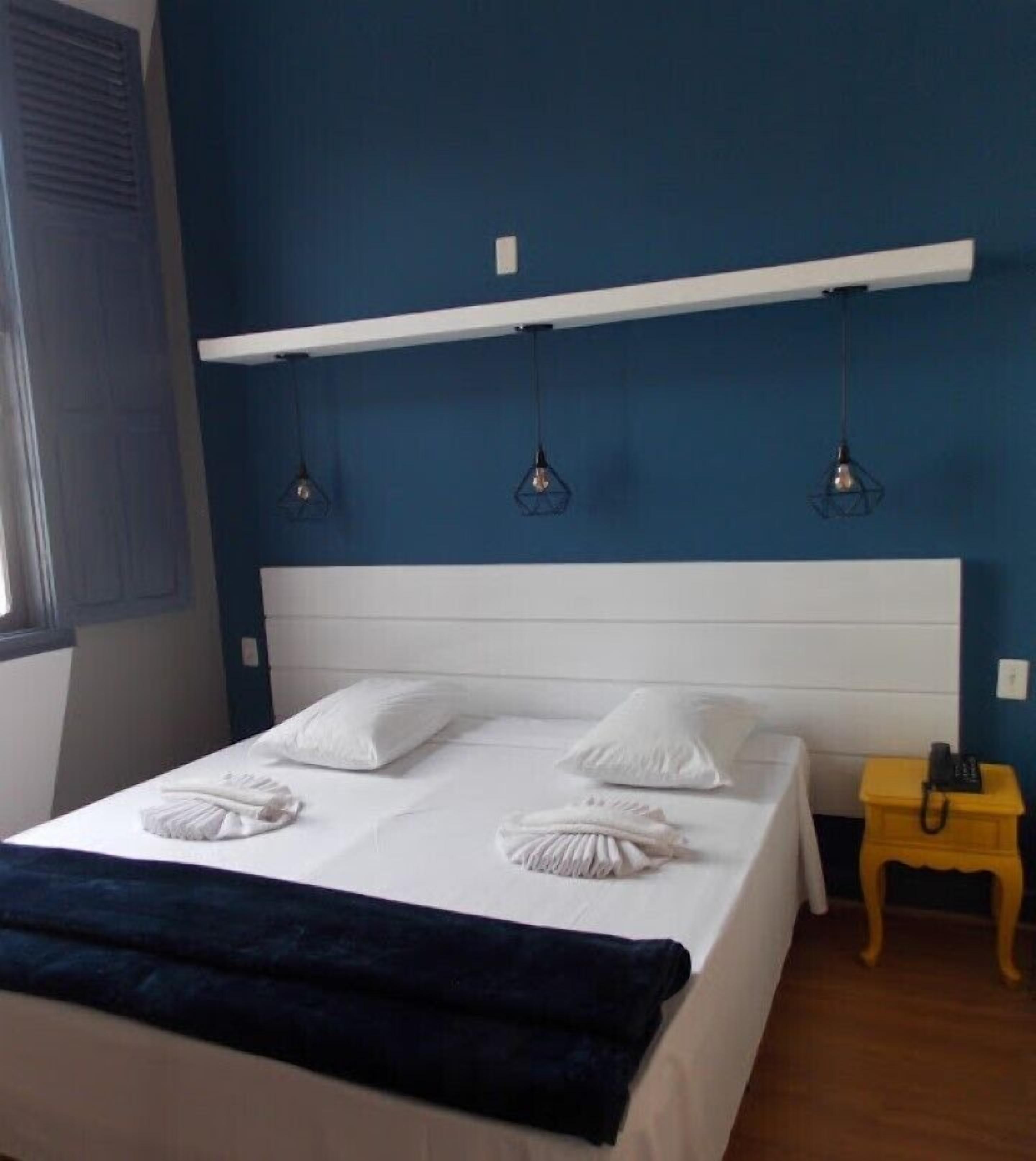 Ein Schlafzimmer mit einem Bett, weißen Kissen, einer dunkelblauen Decke, einem Nachttisch aus Holz und einem Telefon.