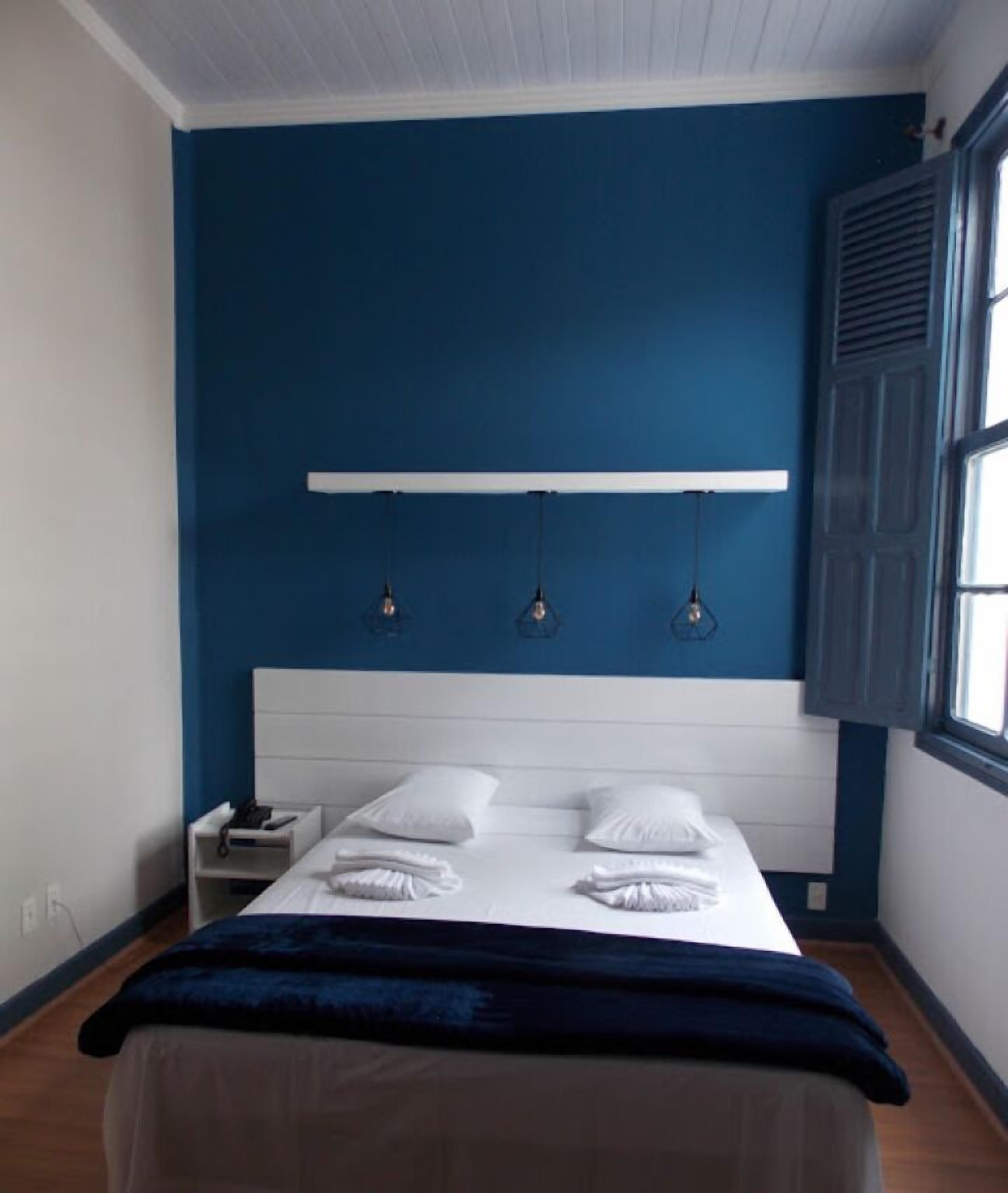 Un dormitorio con una pared azul de acento, un cabecero blanco y una mesita de noche con una lámpara.