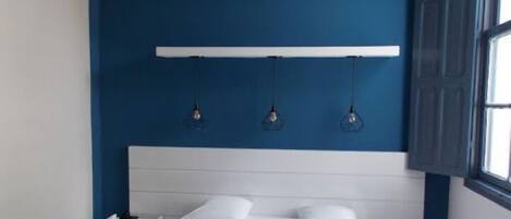 Un dormitorio con una pared azul de acento, un cabecero blanco y una mesita de noche con una lámpara.