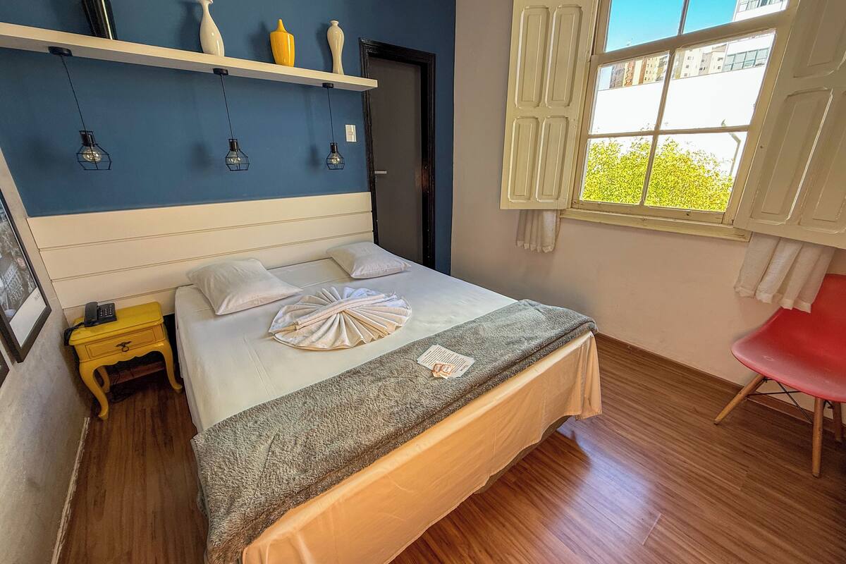 A neatly arranged hotel room with a bed, bedside table, and a window with curtains.