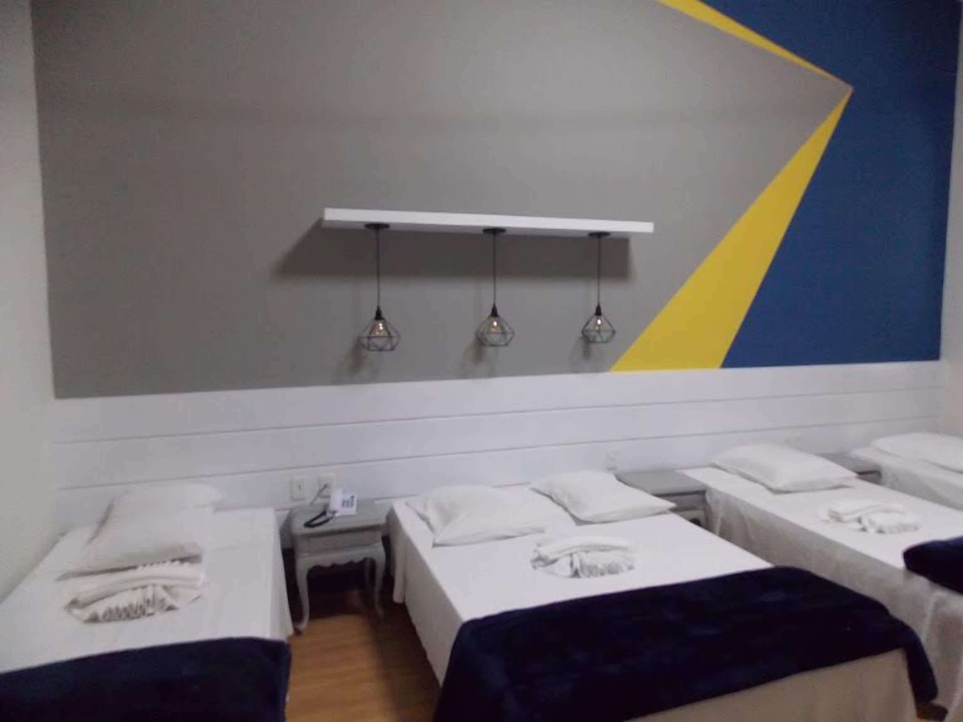 A hotel room with two single beds, a small bedside table with a phone, and a wall-mounted shelf with three pendant lights.
