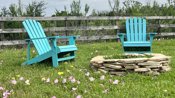 Dos sillas Adirondack turquesa en un campo de hierba, con una valla de madera al fondo.