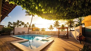 A swimming pool with a wooden deck, surrounded by lounge chairs and palm trees. - Pousada Mariluz (Maragogi)