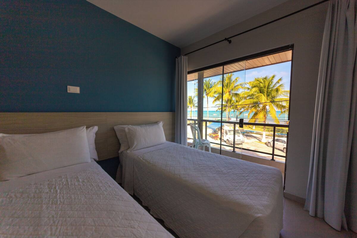 Une chambre d’hôtel avec deux lits, une vue sur les palmiers et la plage, et un balcon avec une balustrade.