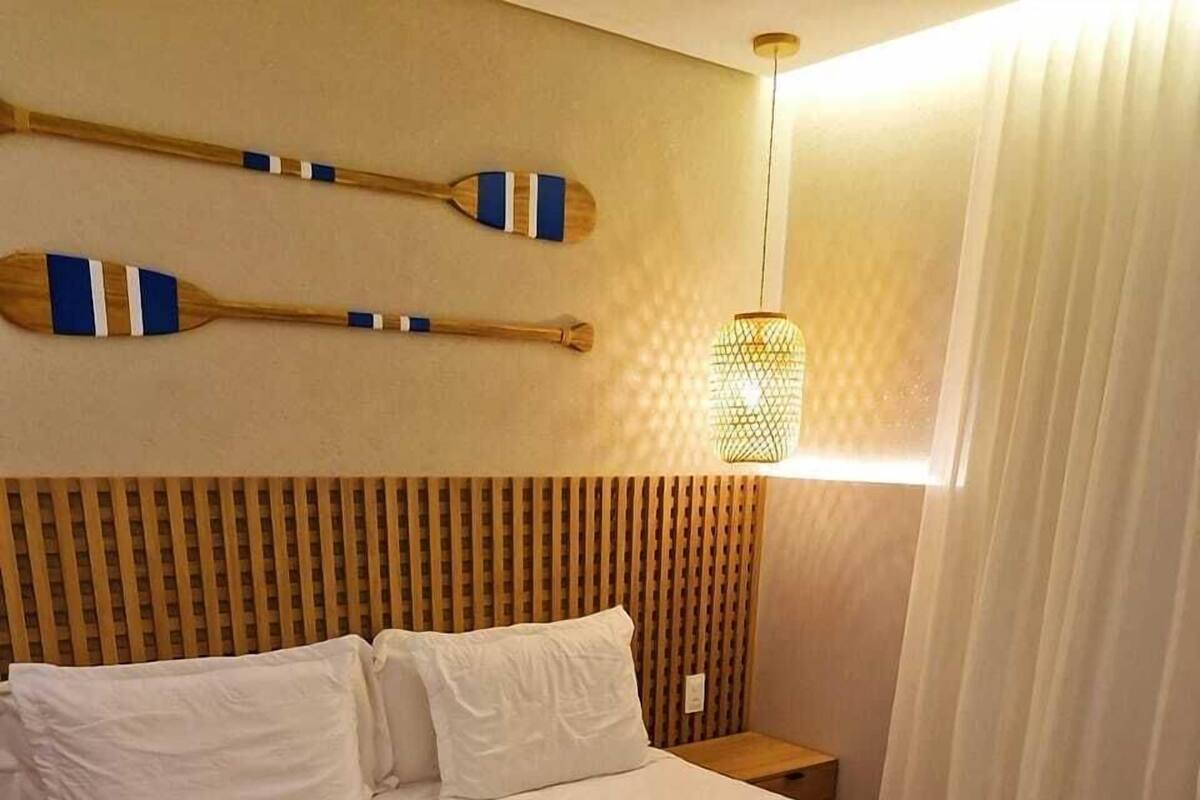 Un lit bien fait, avec une literie blanche et bleu marine, une tête de lit en bois et deux pagaies en bois accrochées au mur.