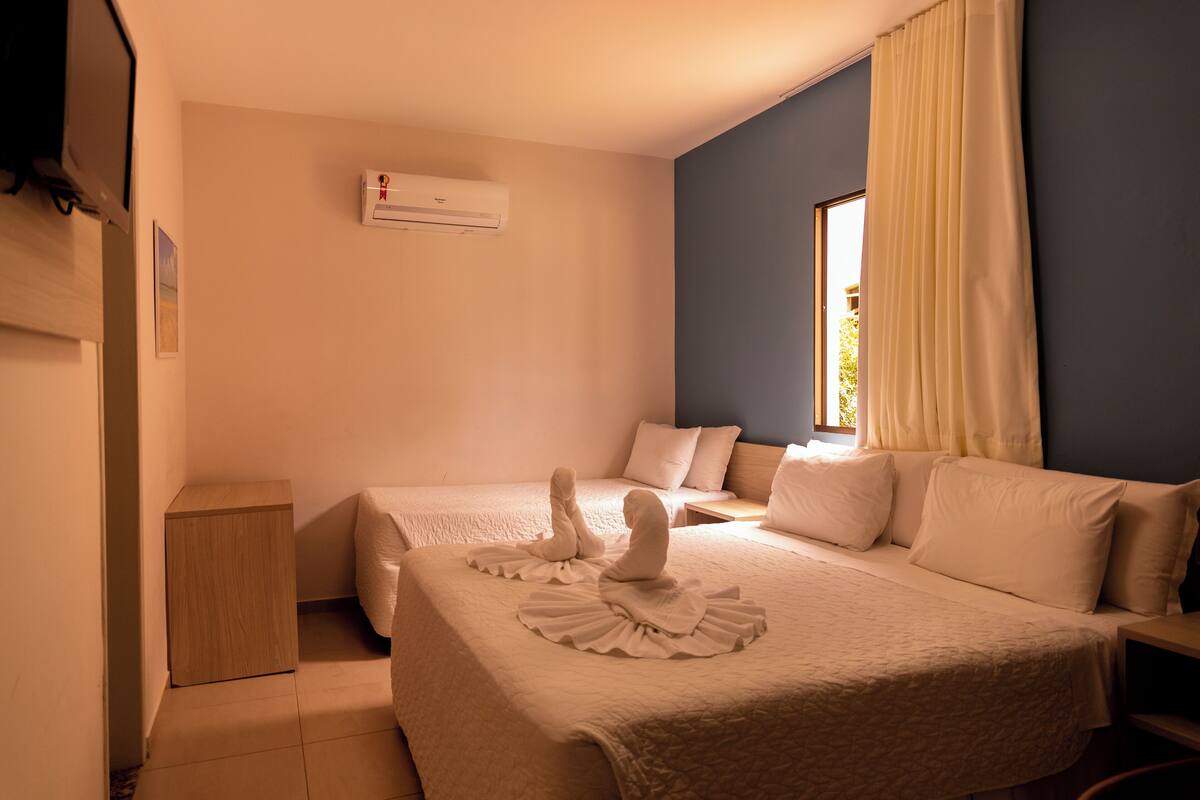 Une chambre d’hôtel avec deux lits, une petite table de chevet en bois, un appareil de climatisation et une fenêtre avec des rideaux.