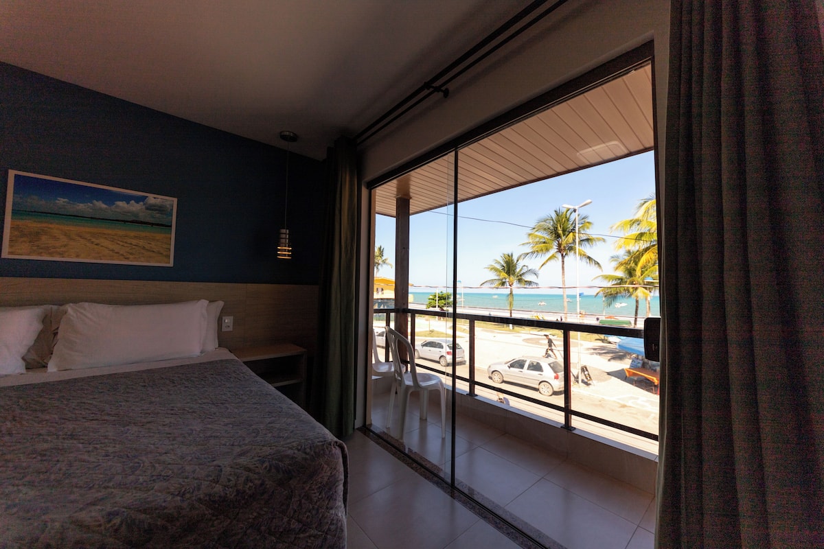 Une chambre d’hôtel dotée d’une grande fenêtre donnant sur la plage et les palmiers.