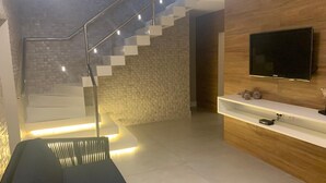 A modern living room with a staircase, a flat-screen TV, and a built-in shelf. - Pousada Mariluz (Maragogi)