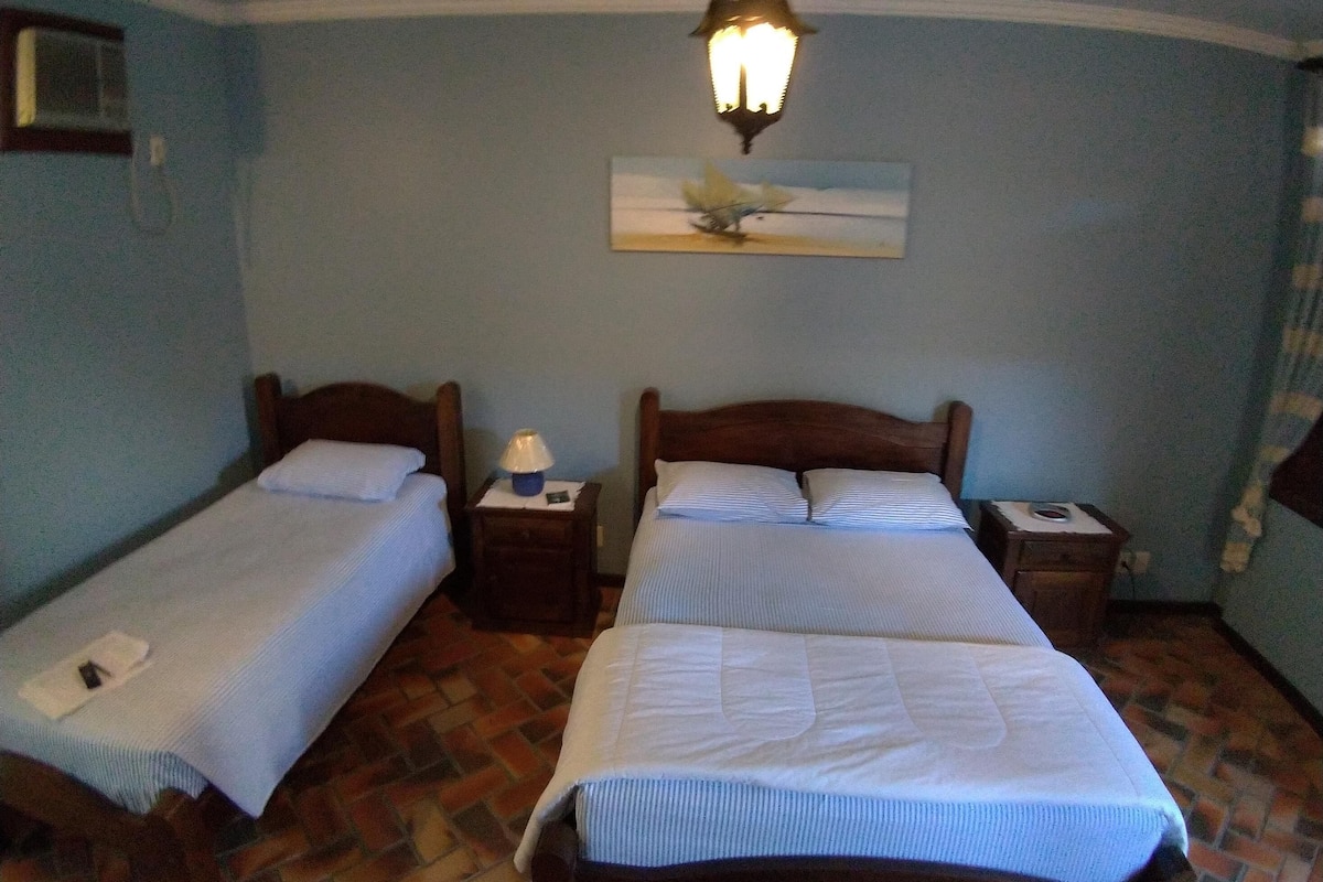 A room with two single beds, a nightstand with a lamp, a painting on the wall, and a patterned floor.