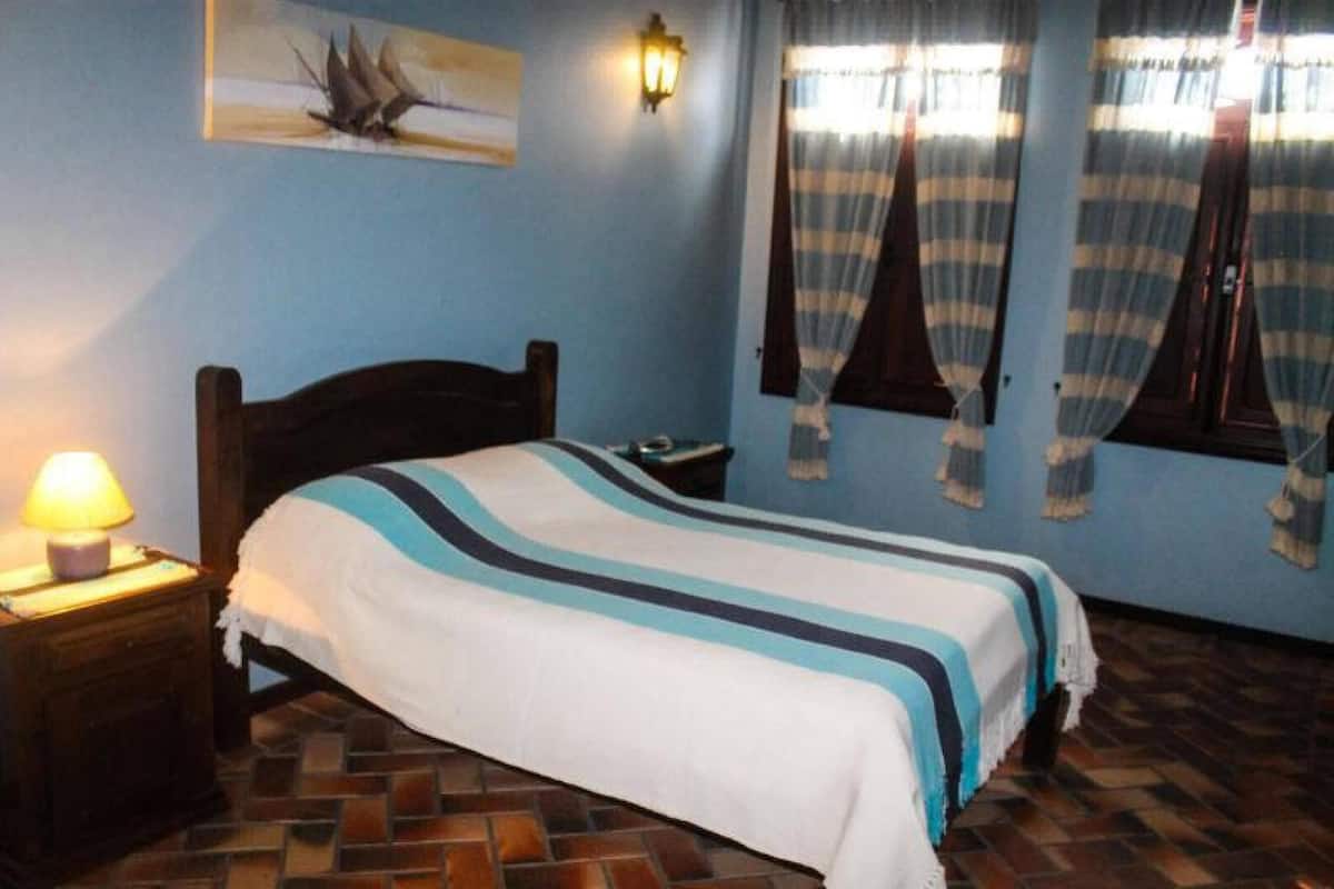 A bedroom with a bed, a nightstand, a wall-mounted lamp, and a window with curtains.