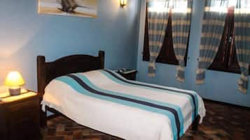 A bedroom with a bed, a nightstand, a wall-mounted lamp, and a window with curtains.