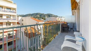 Ein Balkon mit weißen Korbstühlen, einem Tisch und Blick auf eine Hügellandschaft.
