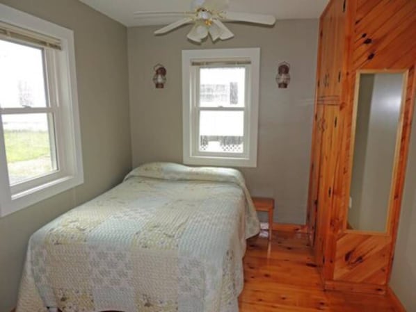 Un dormitorio con cama, ventilador de techo, ventana y paredes de madera.