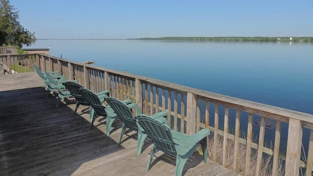 Une terrasse en bois avec des chaises vertes donnant sur un lac paisible.