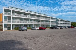Ett hotell med flera våningar, balkonger, en parkeringsplats och ett antal bilar parkerade framför.