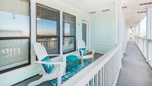 A covered porch with white railings and two white Adirondack chairs with blue cushions.