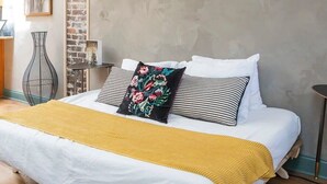 A bedroom with a bed, pillows, a yellow throw blanket, a wall-mounted sign reading "Nashville", and a brick accent wall.