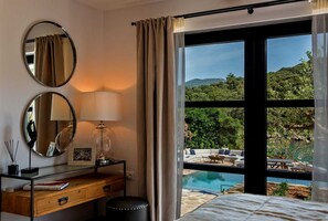 A bedroom with a large window, a desk with a lamp, two round mirrors, and a view of a pool and greenery. - Beachfront Villa Feodora Grande with Pool (Žrnovo)