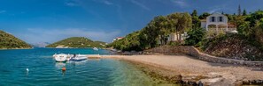 A coastal scene with a stone wall, a white building with a balcony, and boats in the water. - Beachfront Villa Feodora Grande with Pool (Žrnovo)