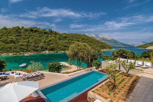 A pool with a view of a coastal area, surrounded by a lounge area with chairs and a sunbed. - Beachfront Villa Feodora Grande with Pool (Žrnovo)