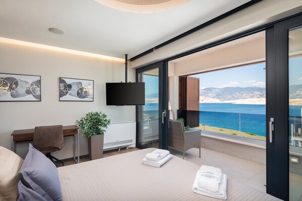 Ein modernes Hotelzimmer mit einem großen Bett, einem Schreibtisch, einem Fernseher und einem Balkon mit Meerblick.