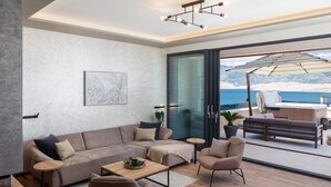 A modern living room with a sofa, armchairs, and a coffee table. There is a large window with a view of the sea and mountains.