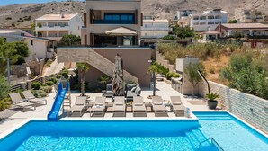 A modern pool area with a slide, lounge chairs, and a staircase leading to a building.
