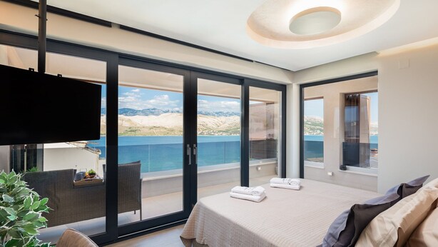 A modern bedroom with a large bed, a TV, and a balcony with a scenic view.