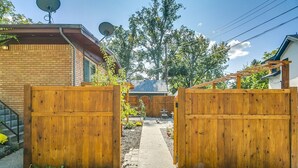A wooden gate leading to a backyard with a patio, a brick wall, and satellite dishes on the roof. - #HabitueHomes - Red Ivy #4 - 2 Bed + Pullout Sofa + Dog Friendly (Boise)