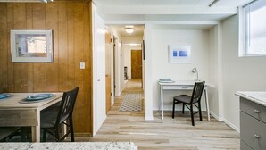 A modern kitchen with a dining area, wooden paneling, a white desk, and a view through a window. - #HabitueHomes - Red Ivy #4 - 2 Bed + Pullout Sofa + Dog Friendly (Boise)