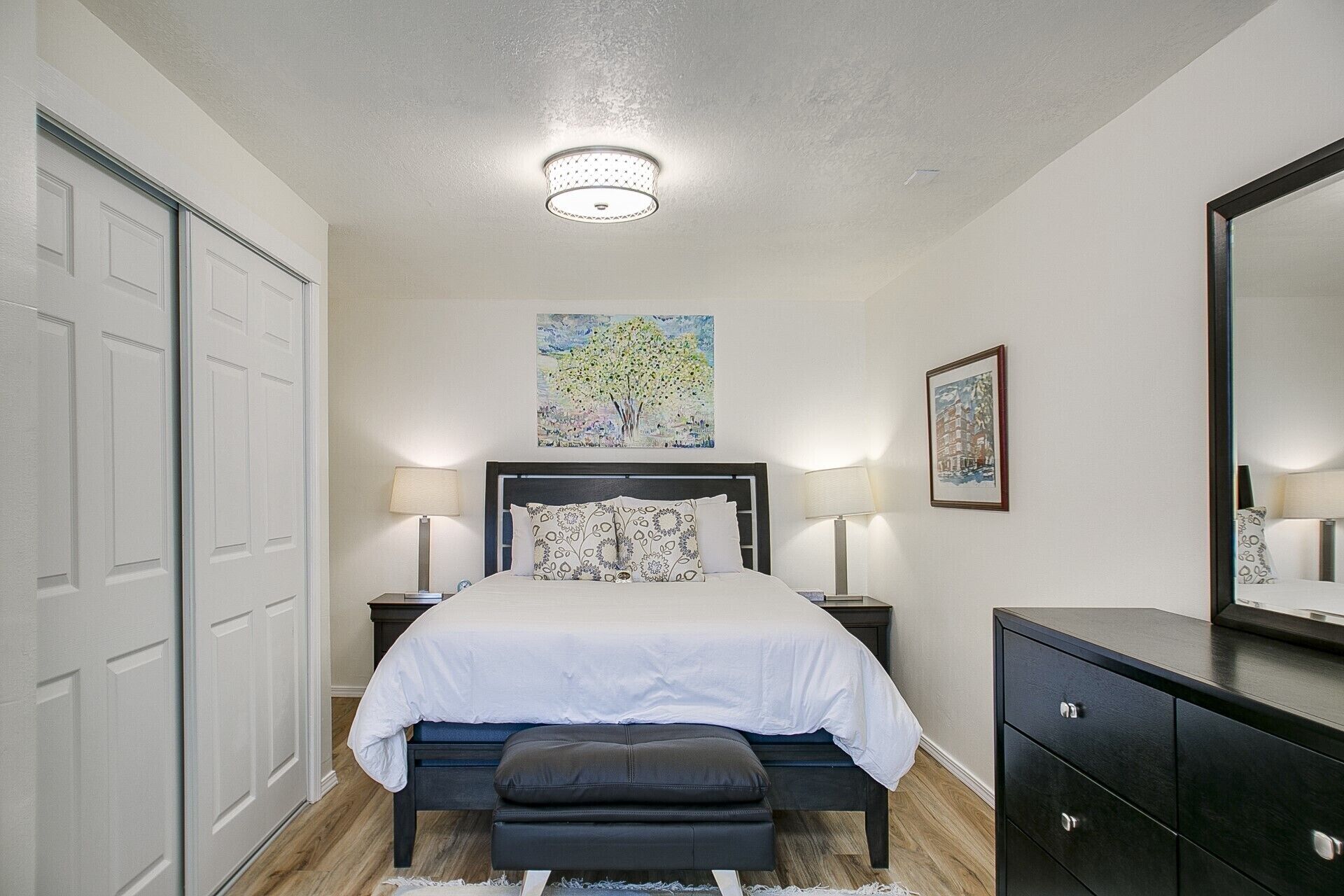 A bedroom with a bed, two bedside tables, a bench, a dresser, and a ceiling light.