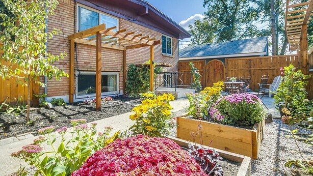 A residential backyard with a wooden pergola, a brick house, a wooden fence, and various flowering plants. - #HabitueHomes - Red Ivy #4 - 2 Bed + Pullout Sofa + Dog Friendly (Boise)