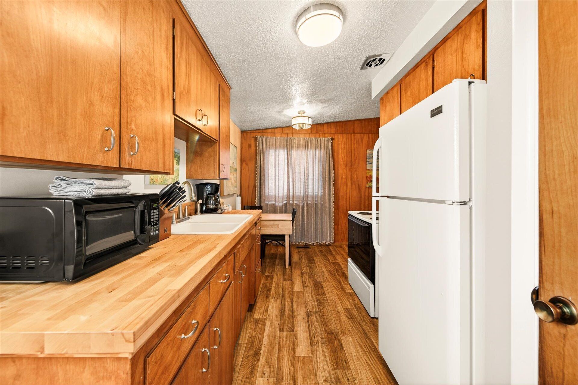 A compact kitchen with wooden cabinets, a microwave, a coffee maker, and a refrigerator.
