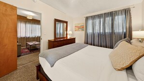 Une chambre d’hôtel avec un lit, une commode, un miroir, un tableau et une porte donnant sur une autre pièce.