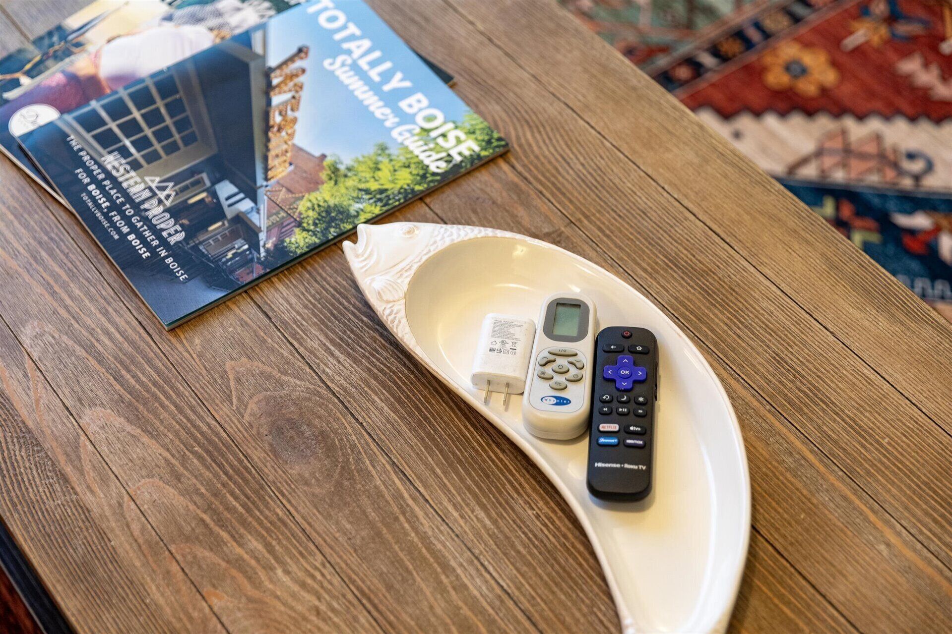 Un libro con el título "Guía Total del Verano en Boise" y un control remoto sobre una mesa de madera.