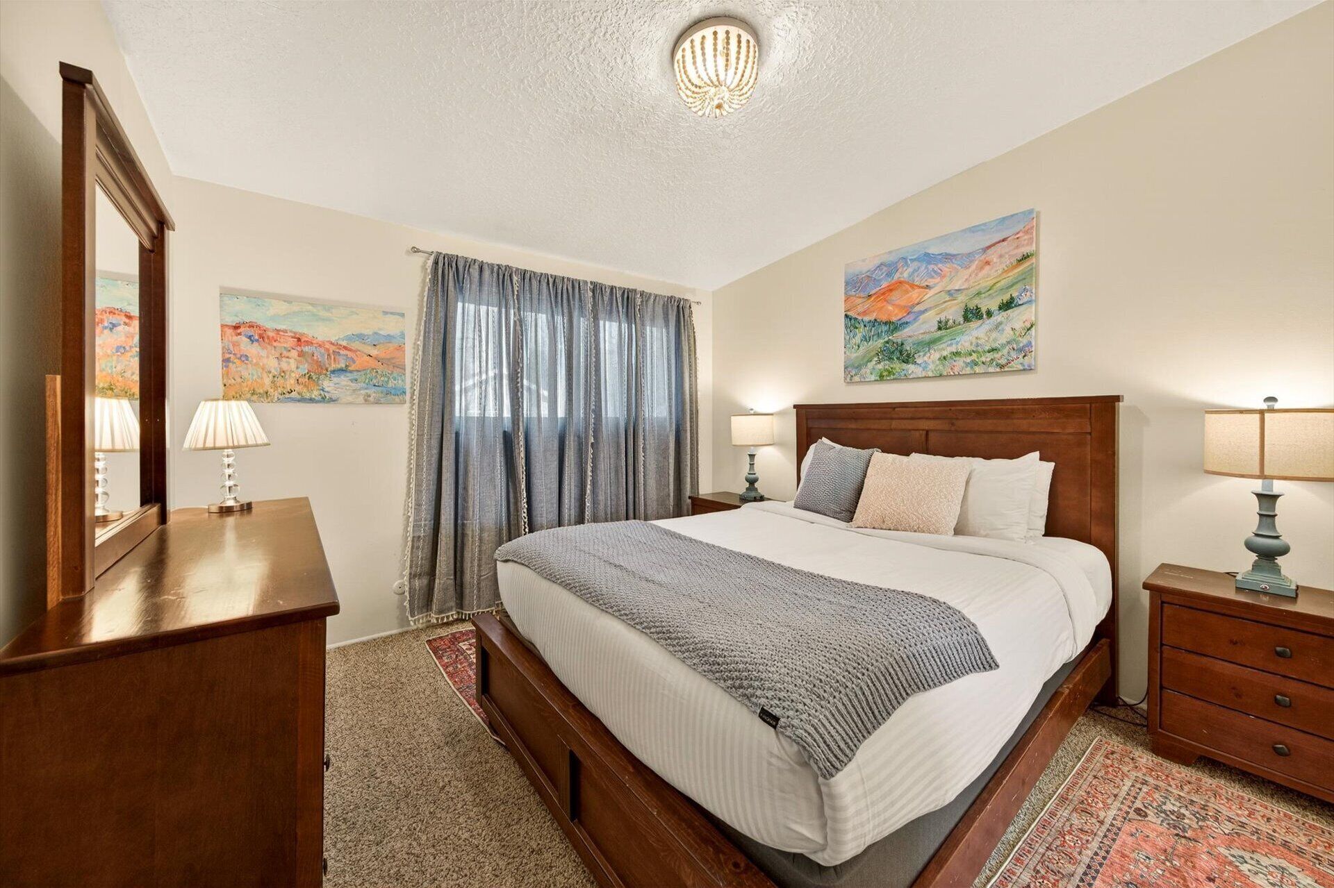 A neatly arranged bedroom with a large bed, two bedside tables, a dresser, and a painting on the wall.