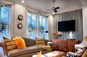 A living room with a sofa, a coffee table, a TV, and a patterned wall. - Rehoboth Guest House - Adults only (Rehoboth Beach)