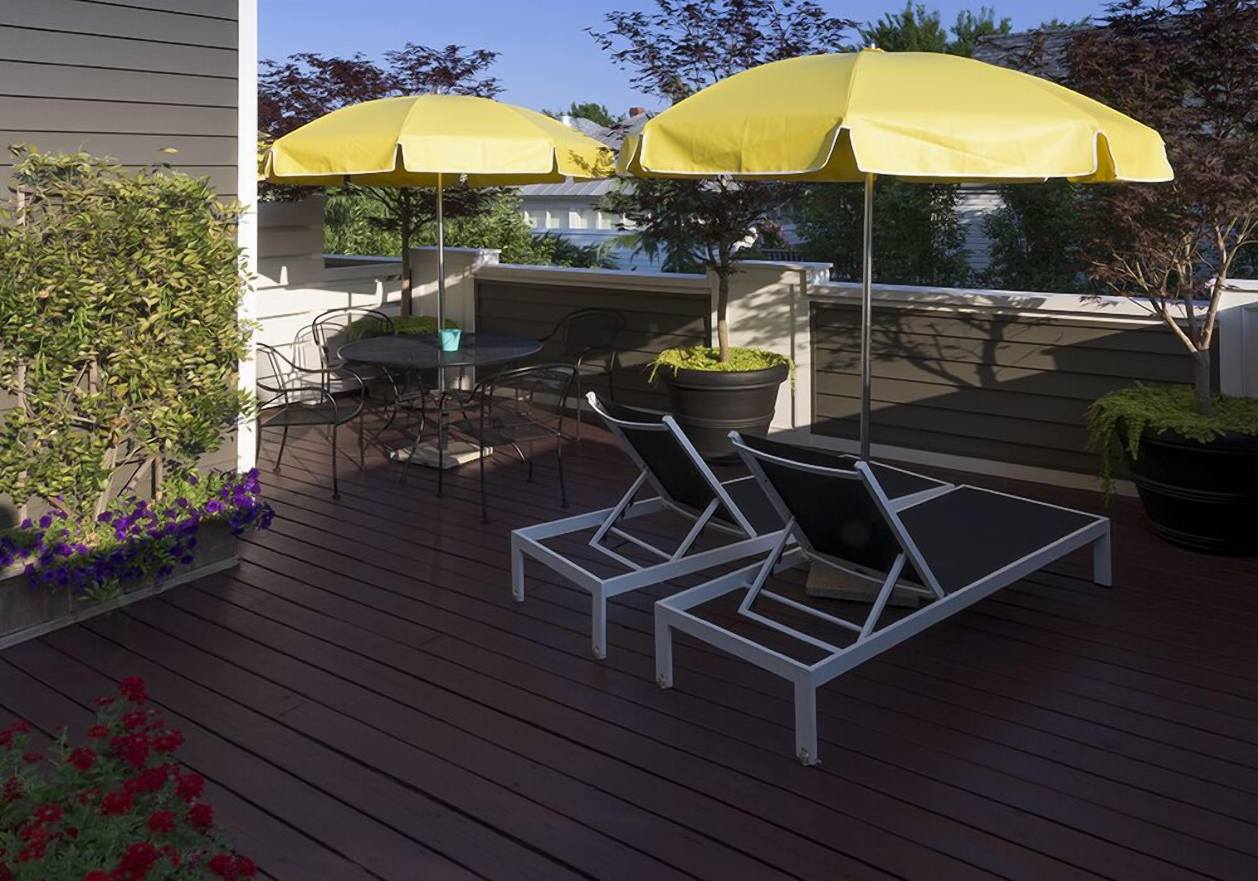 A wooden deck with two yellow umbrellas, a table, and two lounge chairs.