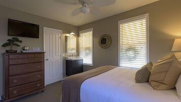 A bedroom with a bed, dresser, ceiling fan, and a TV mounted on the wall.