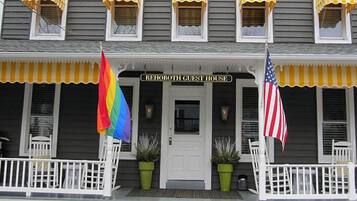 A two-story building with a porch, a sign reading "REHOBOTH GUEST HOUSE", and two flags.