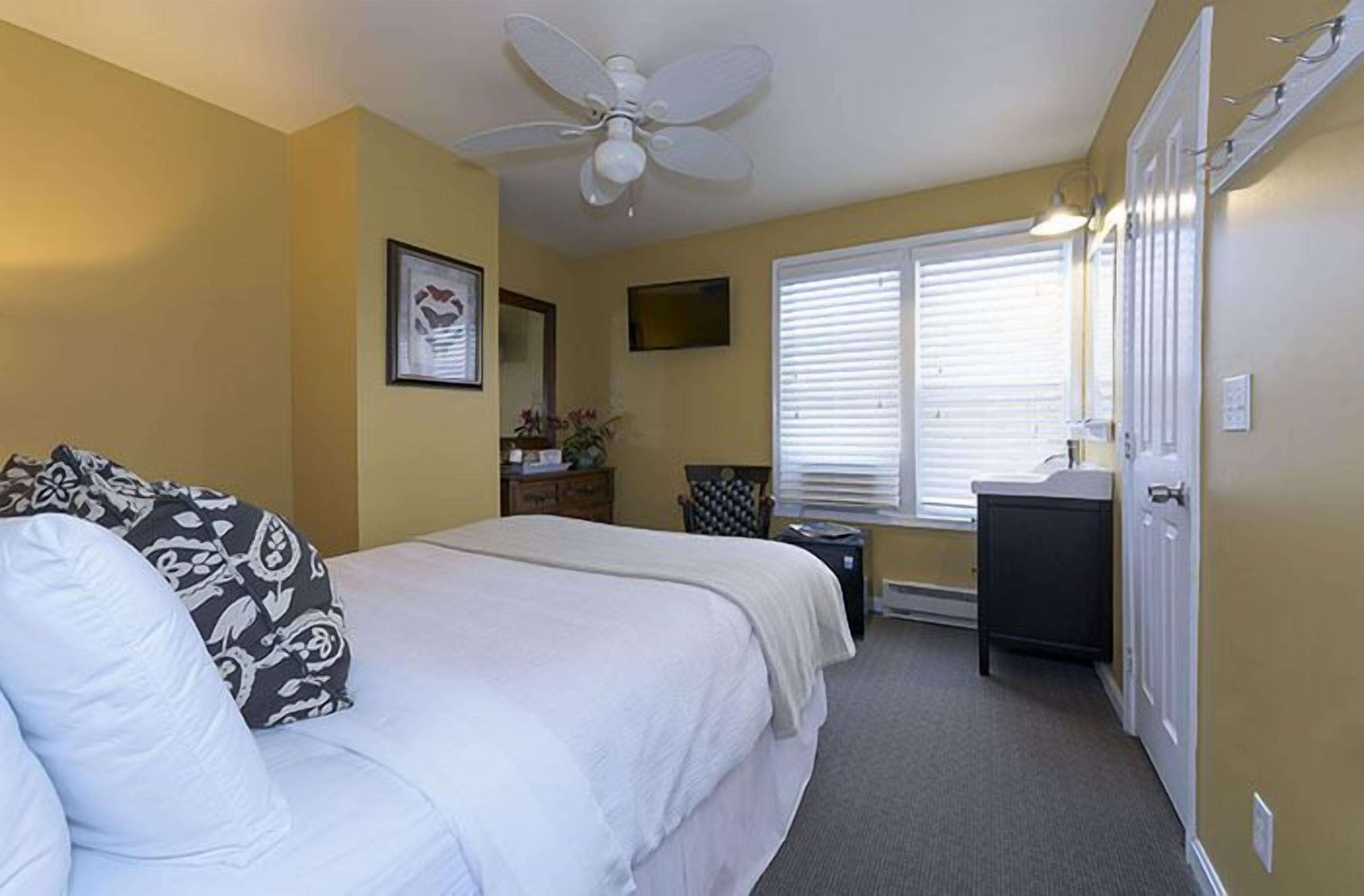 A bedroom with a bed, a desk, a chair, a ceiling fan, and a window with blinds.