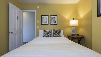 A hotel room with a large bed, two framed pictures on the wall, a bedside lamp, and a door with the number 33.