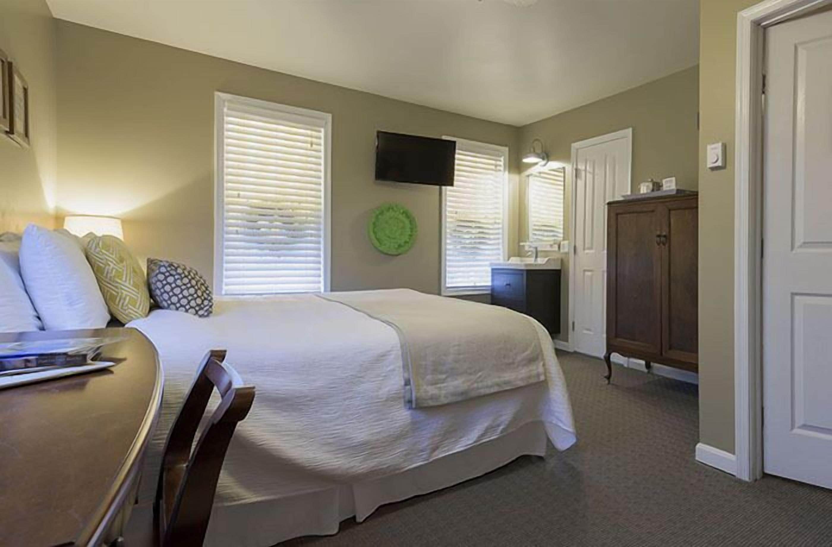 A bedroom with a bed, a desk, a chair, a television, a cabinet, and a door.