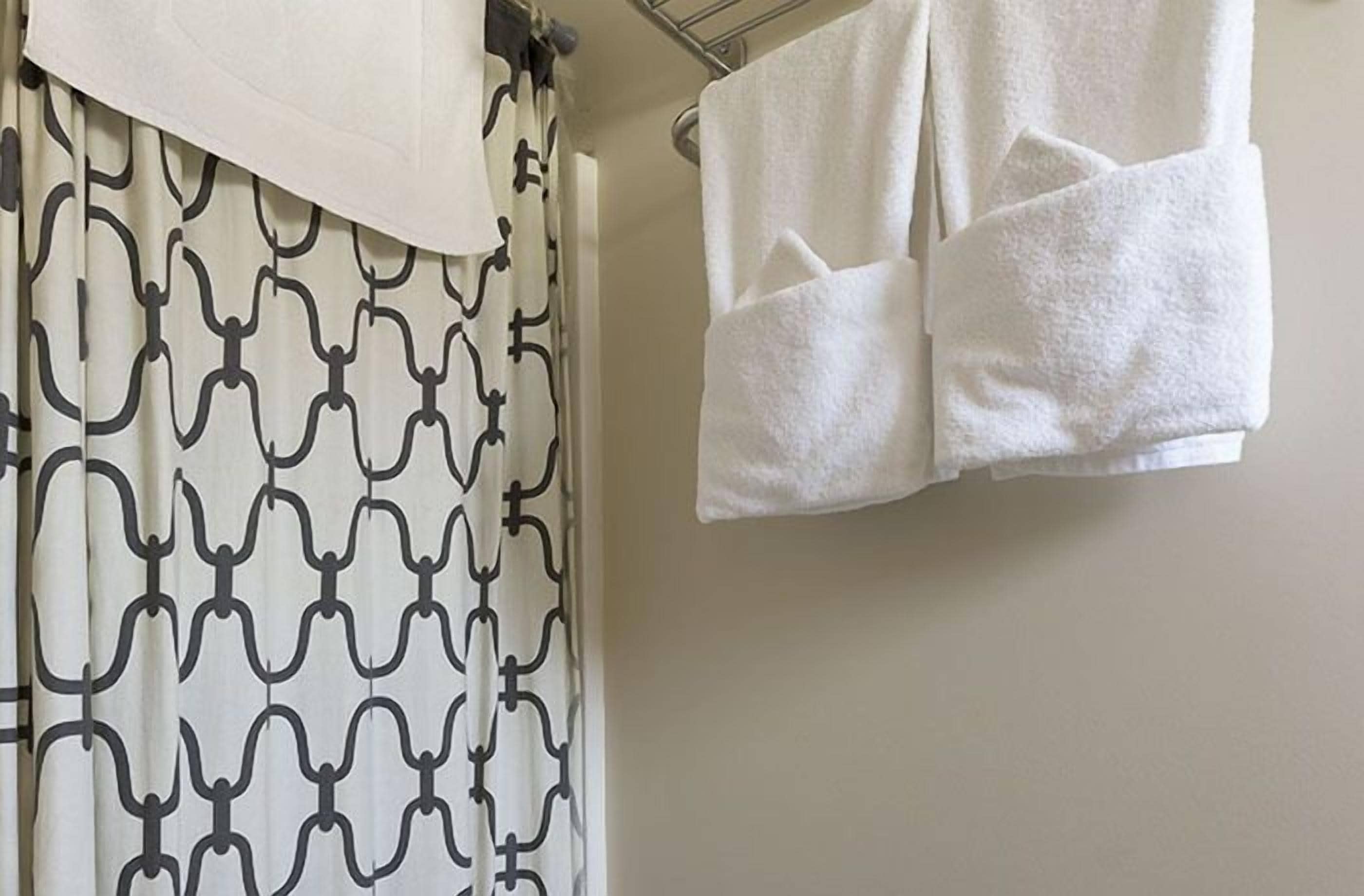 A bathroom with a patterned shower curtain, a towel rack with two towels, and a plain wall.