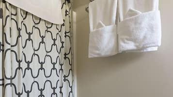 Une salle de bain avec un rideau de douche à motifs, un porte-serviettes avec deux serviettes et un mur uni.