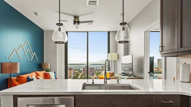 A modern kitchen with a large island, a built-in dishwasher, and a view of the city.